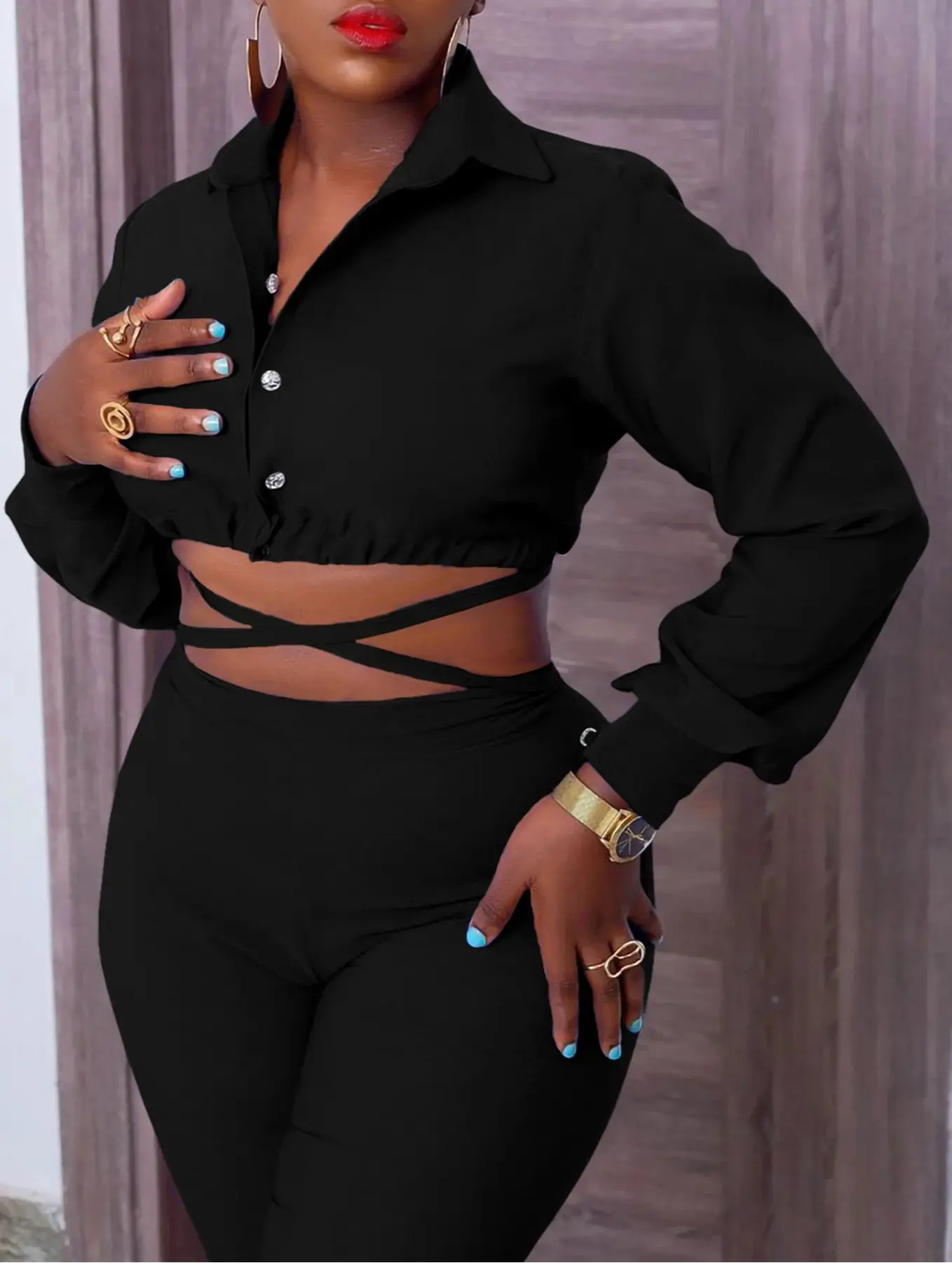 Woman wearing a black outfit with a crop top and high-waisted pants, standing against a neutral background.