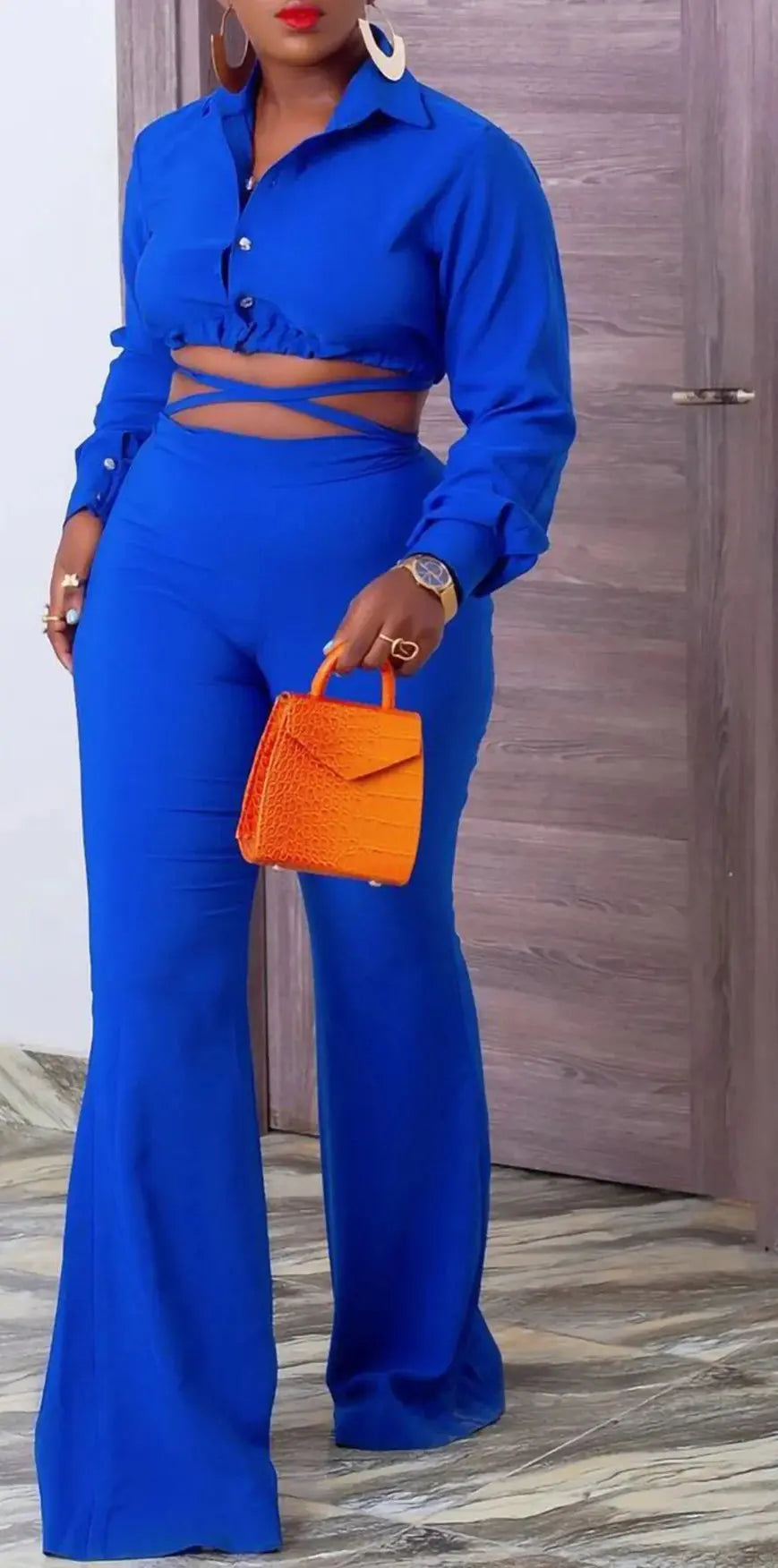Person wearing a blue outfit with a cut-out design, holding an orange handbag indoors.