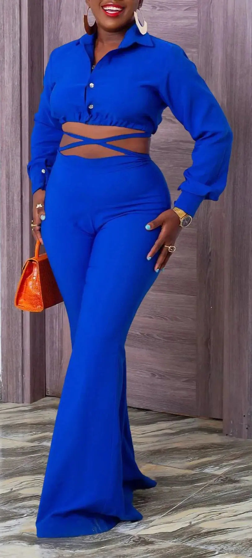Woman in a blue outfit with a brown belt, standing indoors.