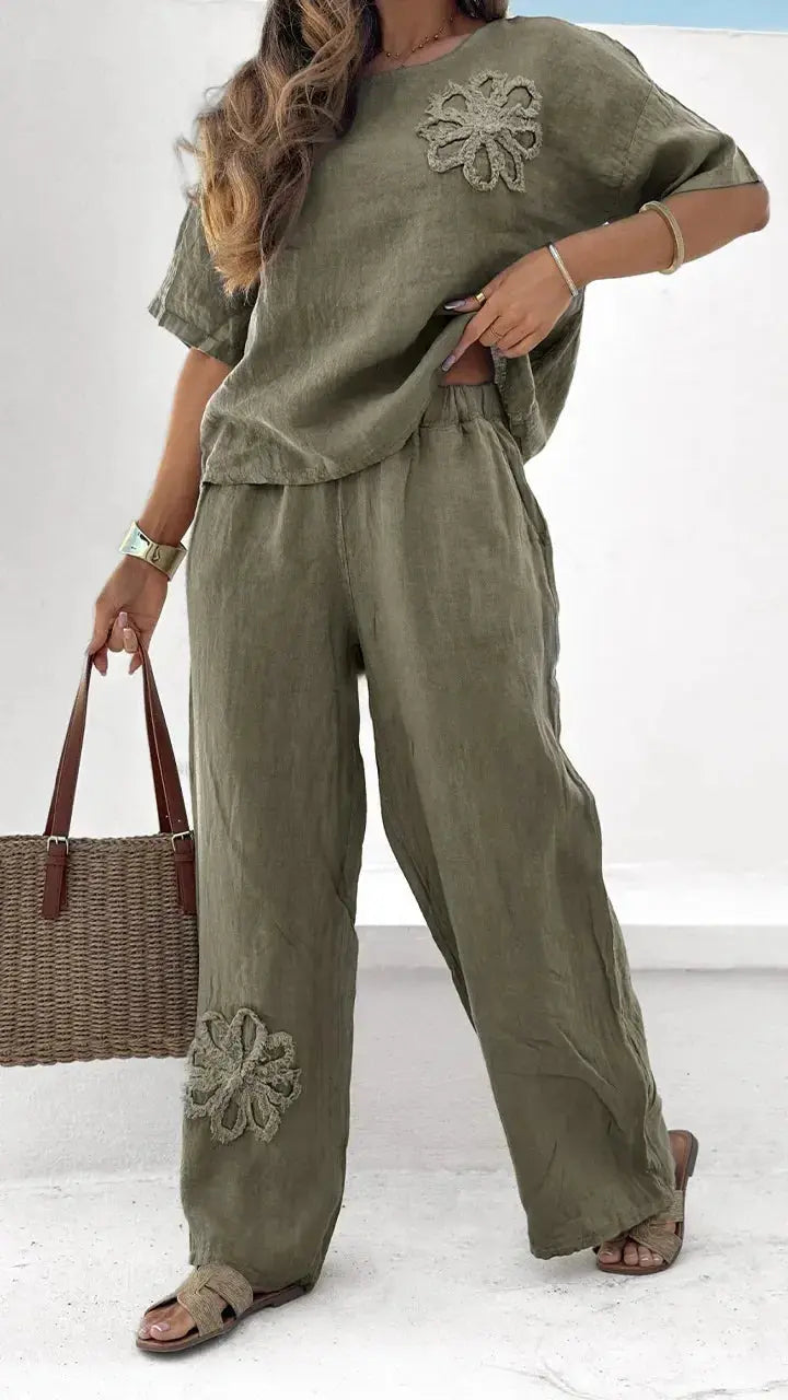 Woman wearing an olive green outfit with floral embroidery, holding a woven bag on a white background