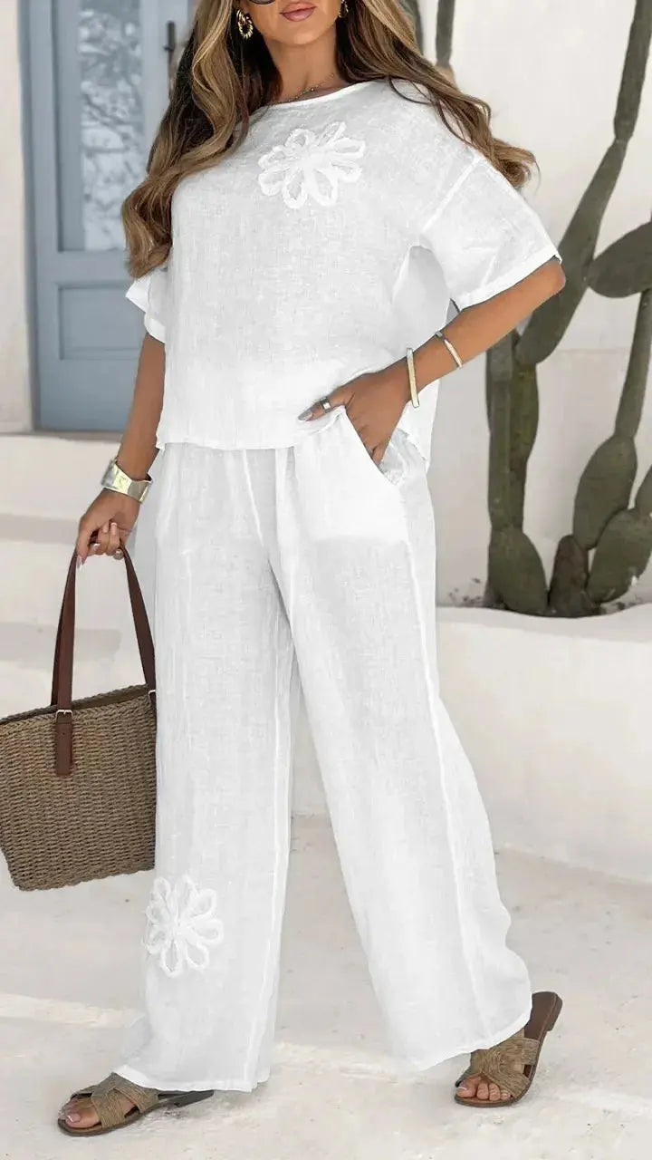Woman wearing a white outfit with floral embroidery, standing indoors.