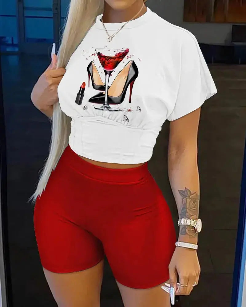 Person wearing a white crop top with a graphic design and red shorts indoors.