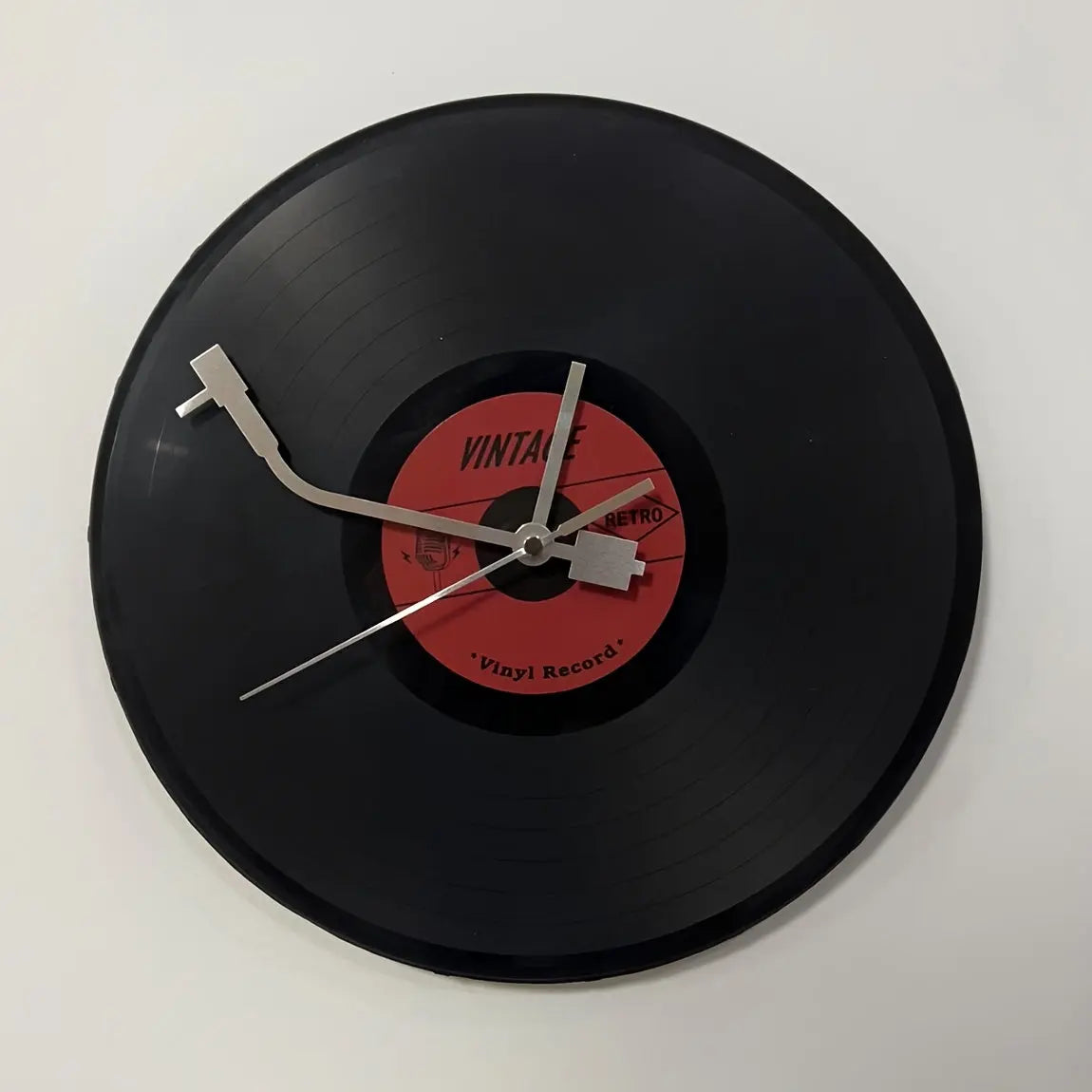 A crisp studio shot of the Time Spinner Vinyl Record Clock by Fantascticz. This detailed view highlights the unique silver tonearm clock hands and the nostalgic red label at the center of the black LP.