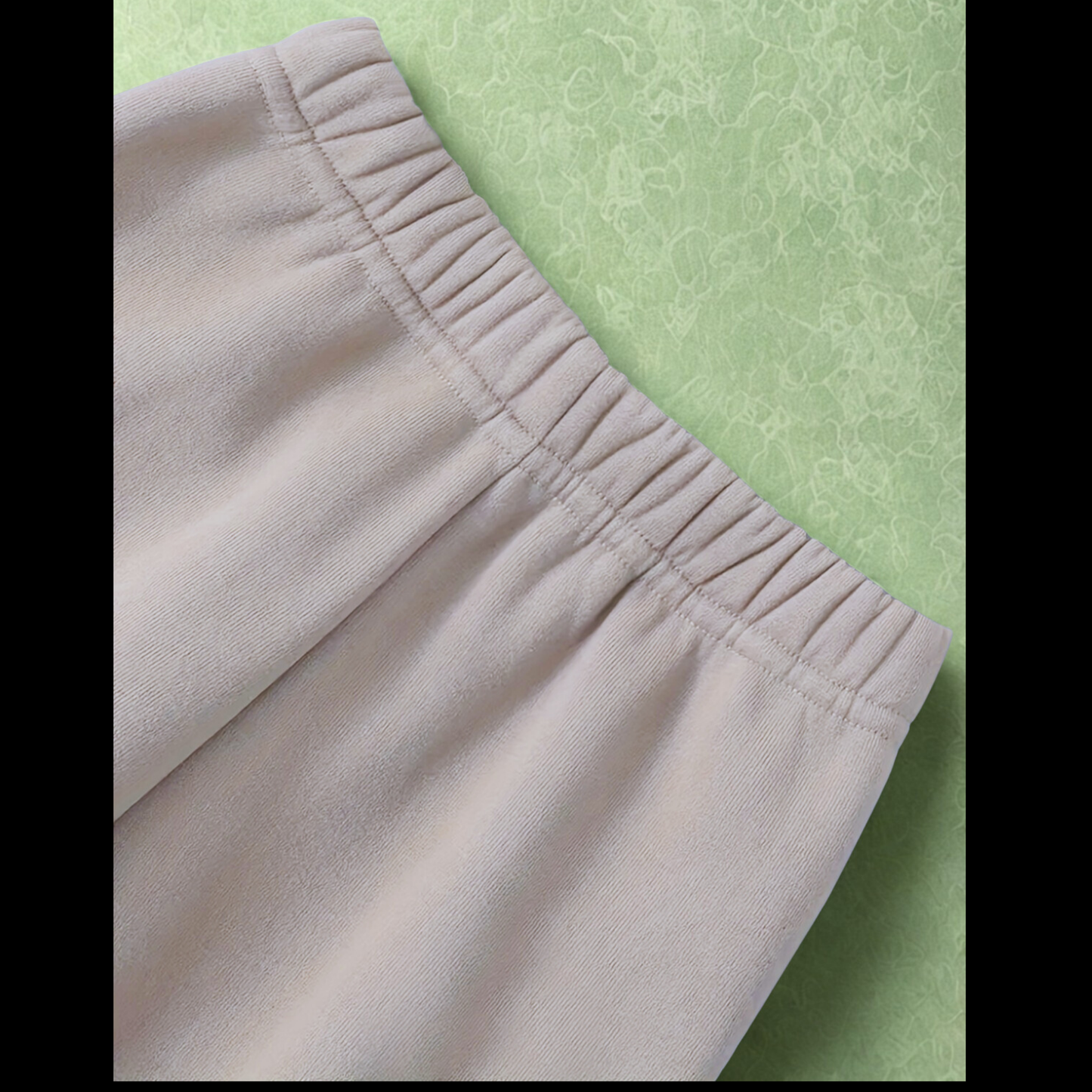 A close-up image showcasing the comfortable, gathered elastic waistband of the beige children's jogger pants against a soft green background.