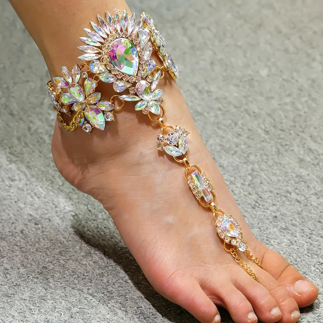 Close-up of The Aurora barefoot sandals on a model's foot, showing the iridescent floral crystal ankle cuff and gold-tone chain detailing.