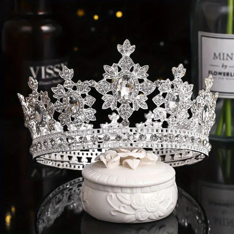 Styled photo of The Sovereign Crown in the Silver & Diamond colorway, featuring a silver-tone frame encrusted with brilliant clear crystals. The crown is displayed on an ornate white trinket box.