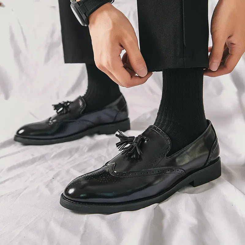 Model wearing The Strummer men's brogue loafers in high-gloss black leather, styled with black trousers.