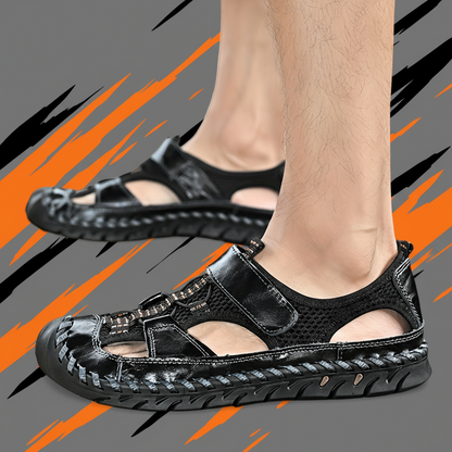 Black sandals worn by a person on a gray background with orange and black abstract designs.