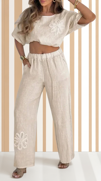 Woman wearing a beige outfit with floral embroidery against a wooden panel background