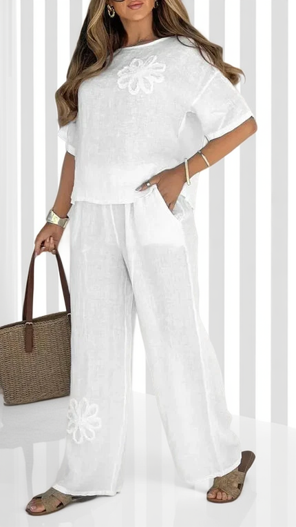 Woman wearing a white outfit with floral details, holding a woven bag against a white background