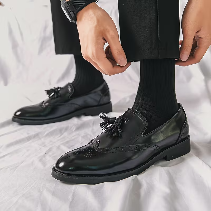 Person wearing black dress shoes with tassels on a white background