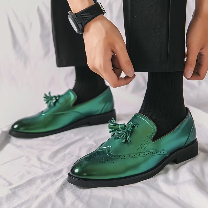 Green shiny dress shoes with tassels worn by a person on a white background