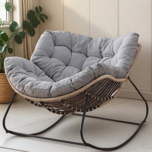 Side view of The 'Oasis' Ergonomic Rocking Lounger from Fantascticz. The chair has a thick, tufted gray cushion and sits on a modern black metal rocking frame with a natural woven base.