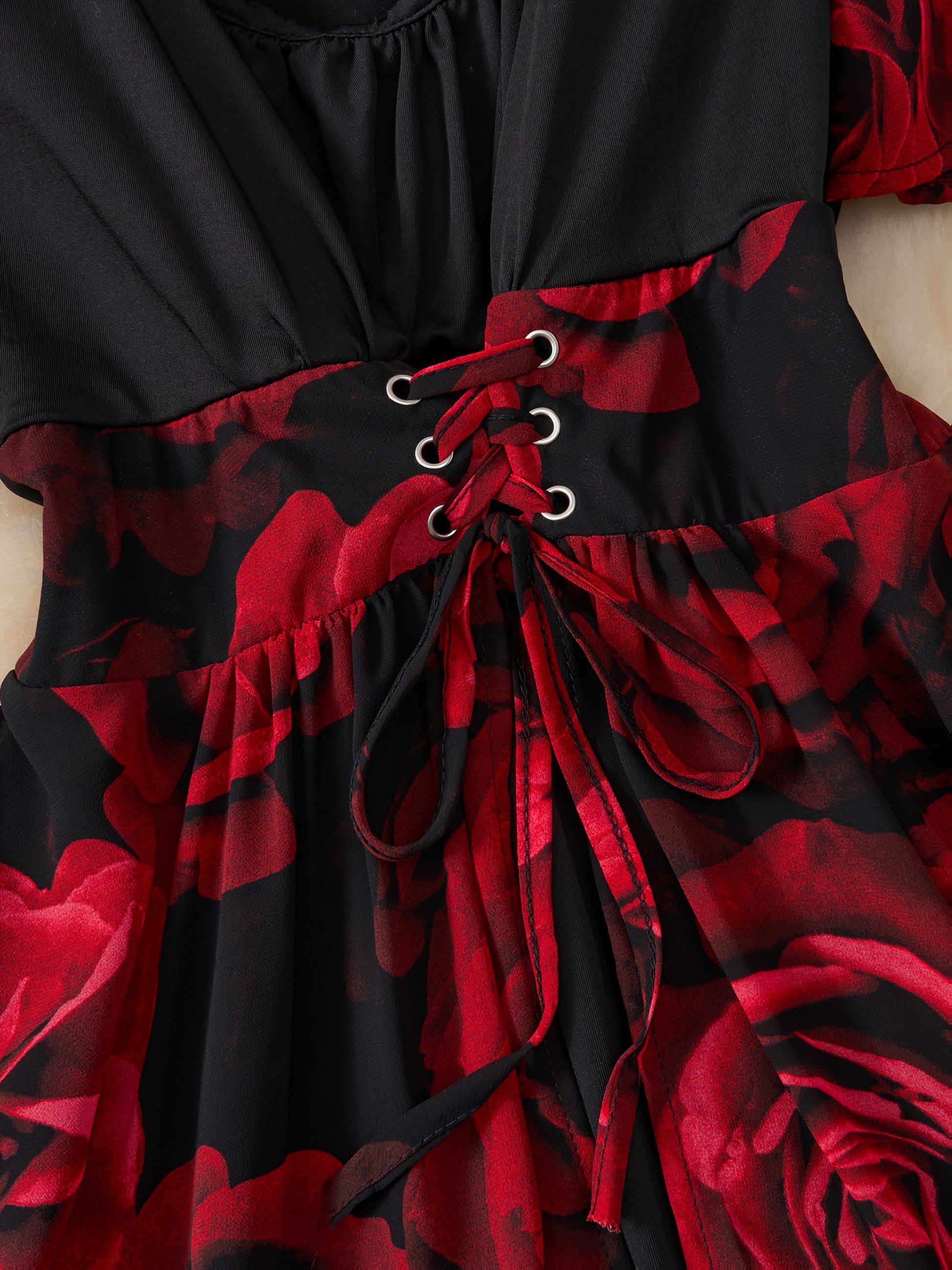 Black dress with red floral pattern and lace-up front on a mannequin.