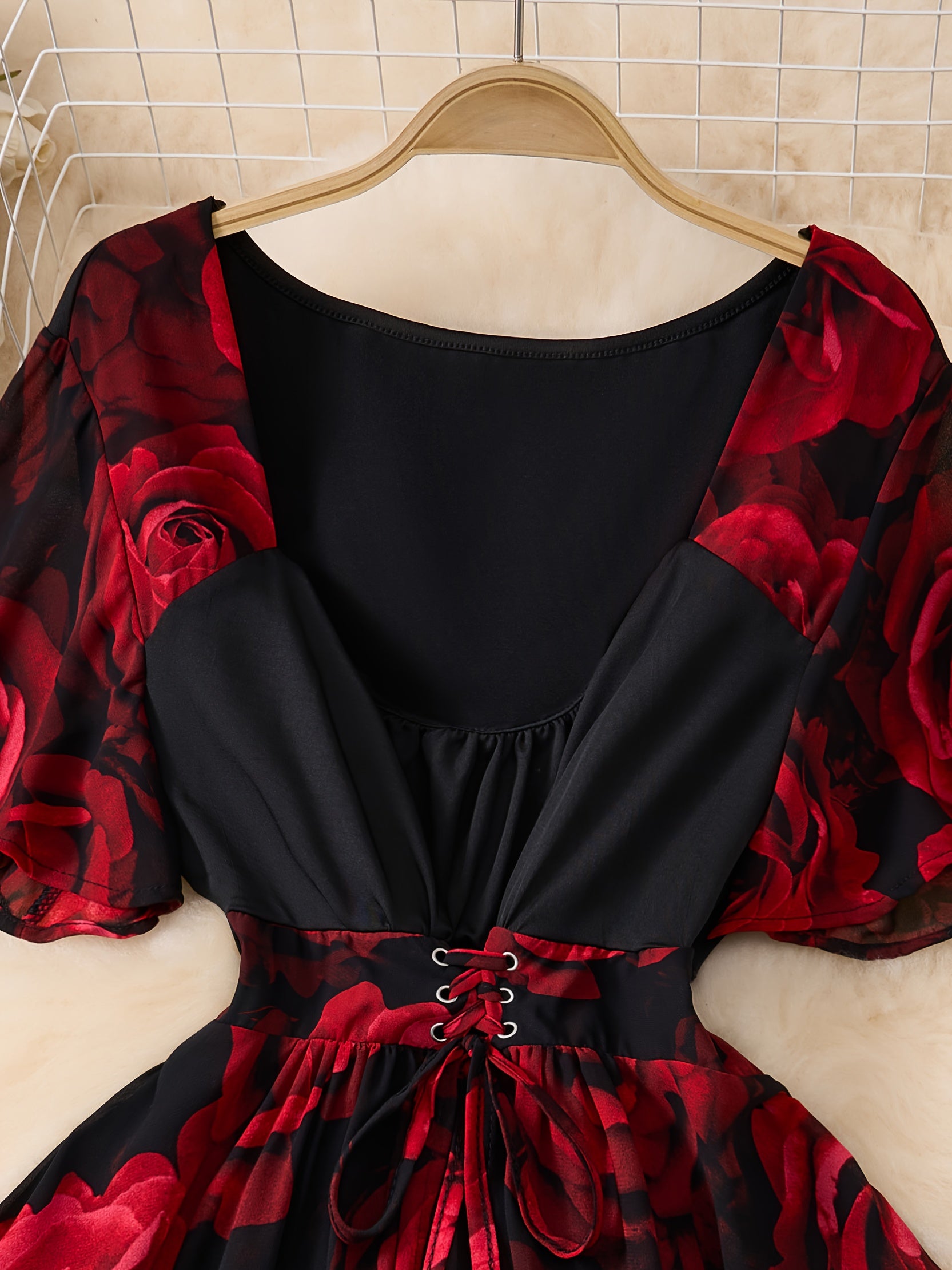 Black dress with red floral sleeves on a hanger against a tiled wall.