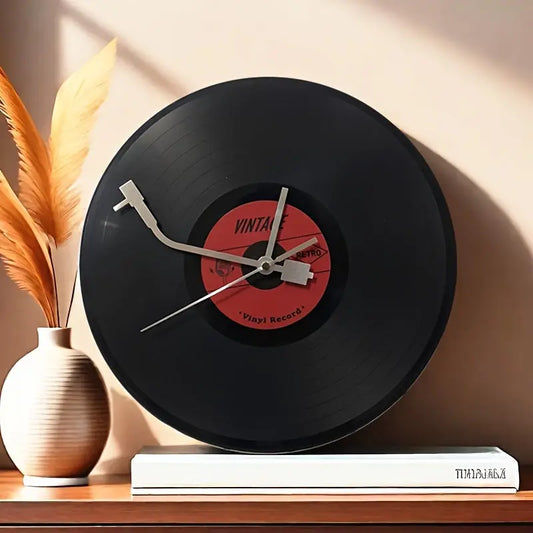 The Time Spinner Vinyl Record Clock by Fantascticz, styled on a wooden shelf. The unique clock hands are designed to look like a silver turntable tonearm on a classic black LP record.


