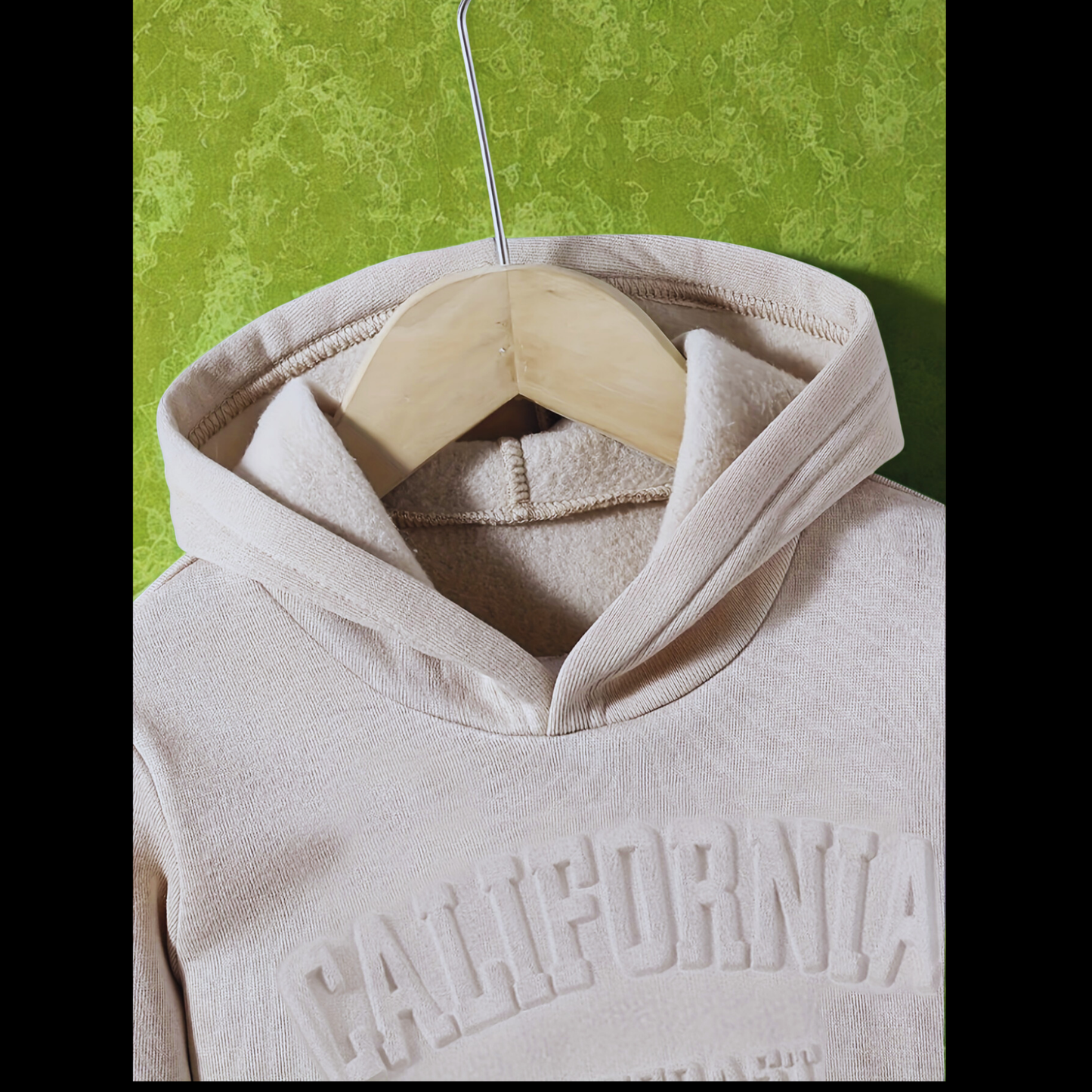 A close-up shot of a beige hoodie on a wooden hanger, showcasing the soft fleece-lined hood and the embossed 'CALIFORNIA' lettering on the chest.