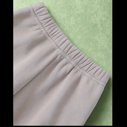 A close-up image showcasing the comfortable, gathered elastic waistband of the beige children's jogger pants against a soft green background.