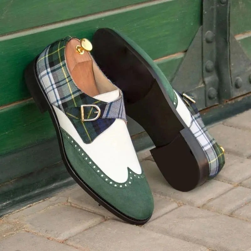 Lifestyle photo of The Sinclair Loafers, showcasing their distinctive green suede, white leather, and classic plaid pattern. One shoe leans against a dark green door, displaying its sole.

