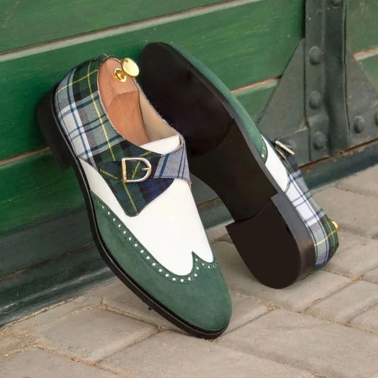 Lifestyle photo of The Sinclair Loafers, showcasing their distinctive green suede, white leather, and classic plaid pattern. One shoe leans against a dark green door, displaying its sole.

