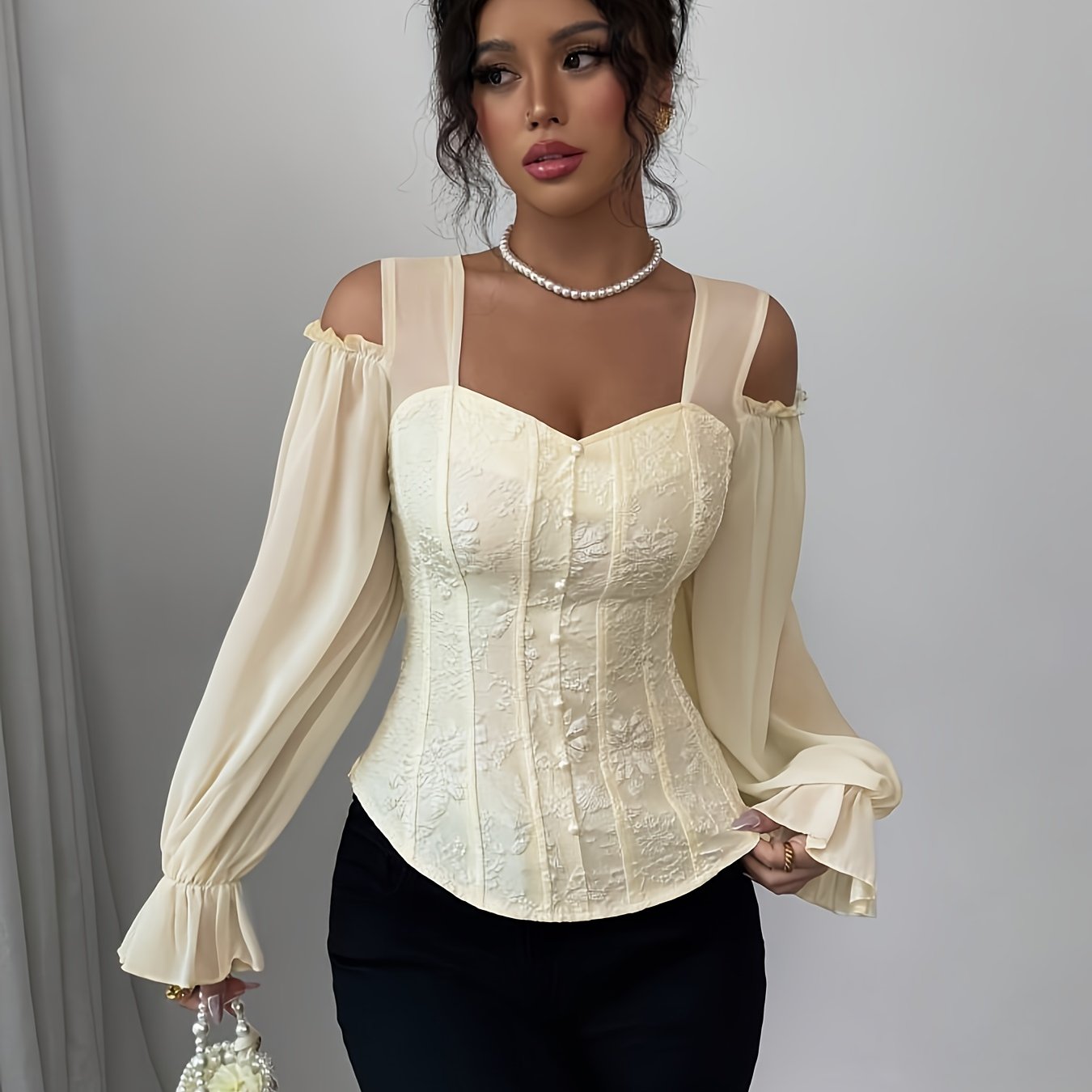 A woman wearing a cream-colored corset-style blouse with sheer sleeves against a gray background.