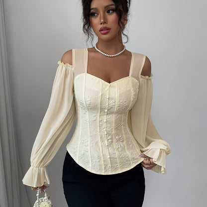 A woman wearing a cream-colored corset-style blouse with sheer sleeves against a gray background.