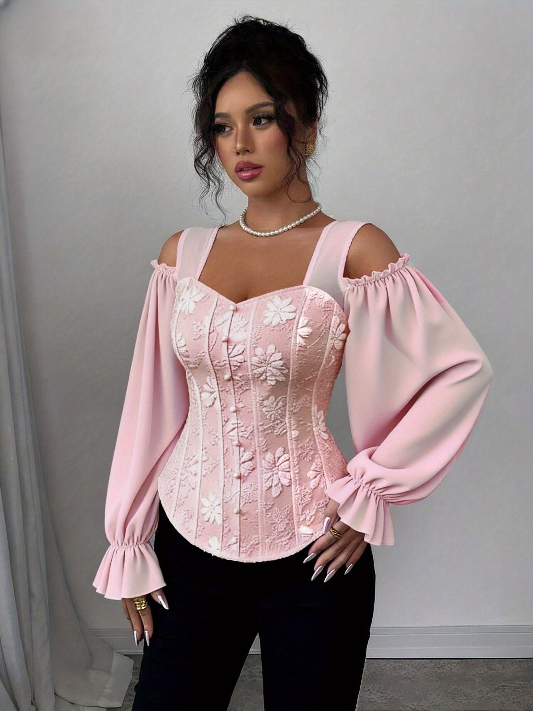 A woman wearing a pink lace corset style top with long sleeves against a plain background