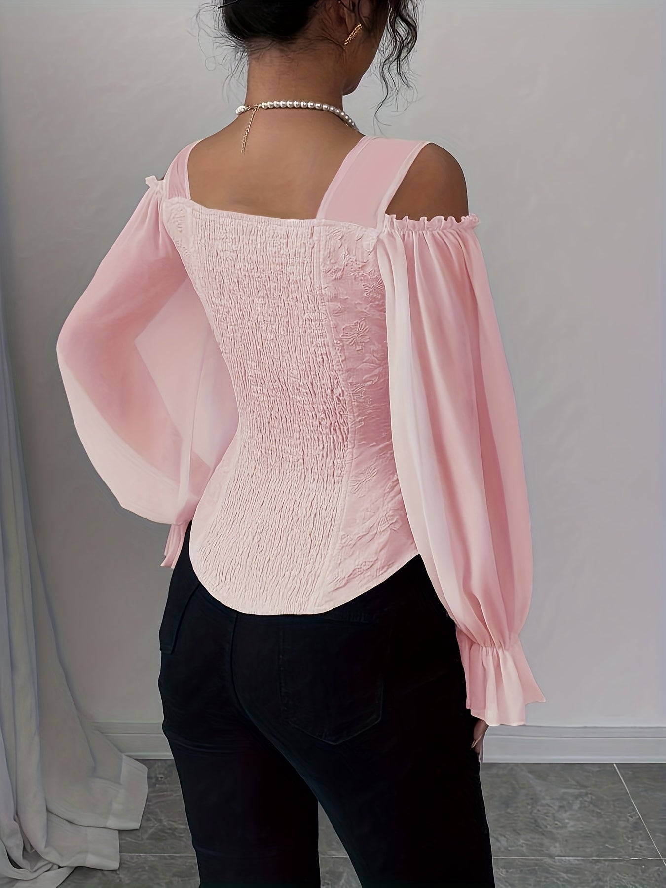 Person wearing a light pink corset style blouse with sheer sleeves against a neutral background