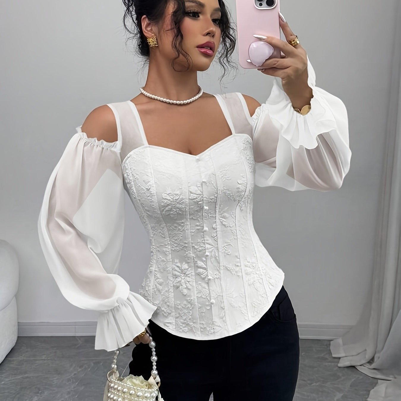 A woman wearing a white corset-style lace top with sheer sleeves, holding a phone and a small bag.